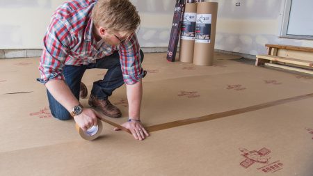 A man on the floor using duct tape to connect various protective surfaces.